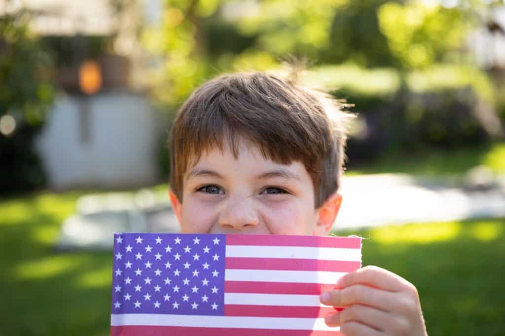 young boy outside holding a US flag and smiling